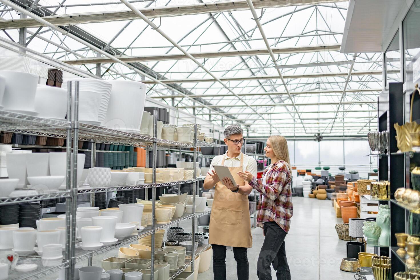 A shop assistant discusses plant pots with a customer in a store. The shelves are filled with diverse, stylish flowerpots. photo
