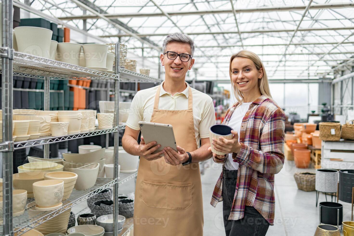 A shop employee helps a customer select flowerpots in a garden center, surrounded by various plant containers. photo