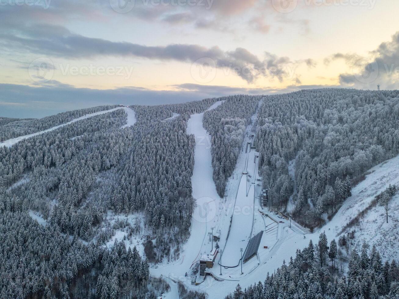 Snow-covered hills surround the Jested Ski resort in Liberec, Czechia. Ski jumps are visible, showcasing the winter sports activities popular in this scenic landscape. photo