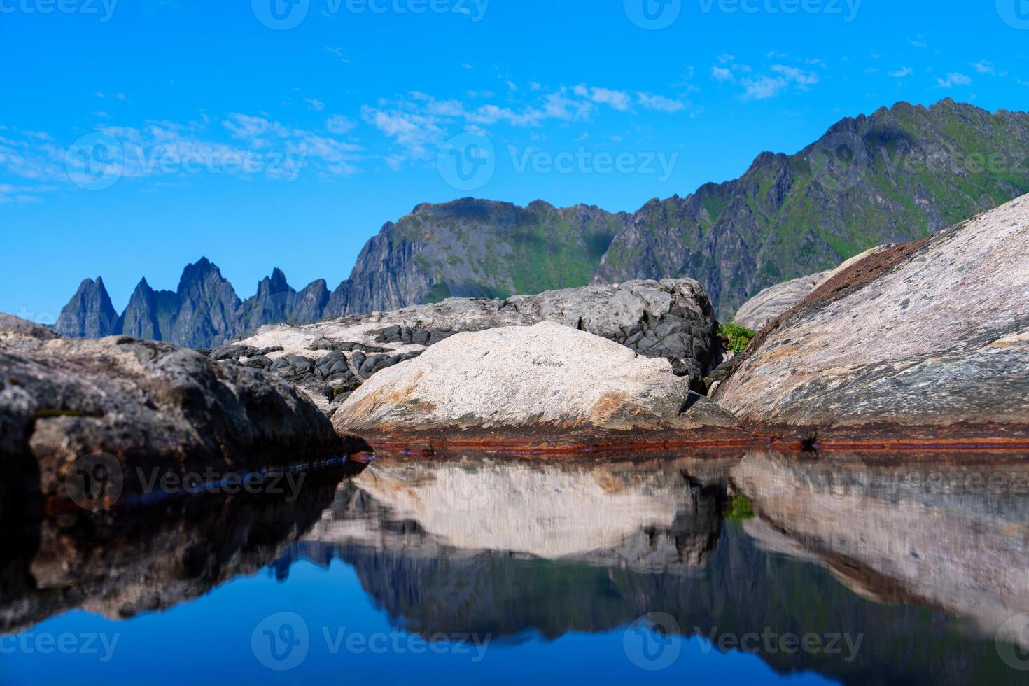 A breathtaking scene of a Norwegian fjord on a sunny day, with tranquil waters, majestic mountains, and a clear blue sky reflecting on the serene sea. photo