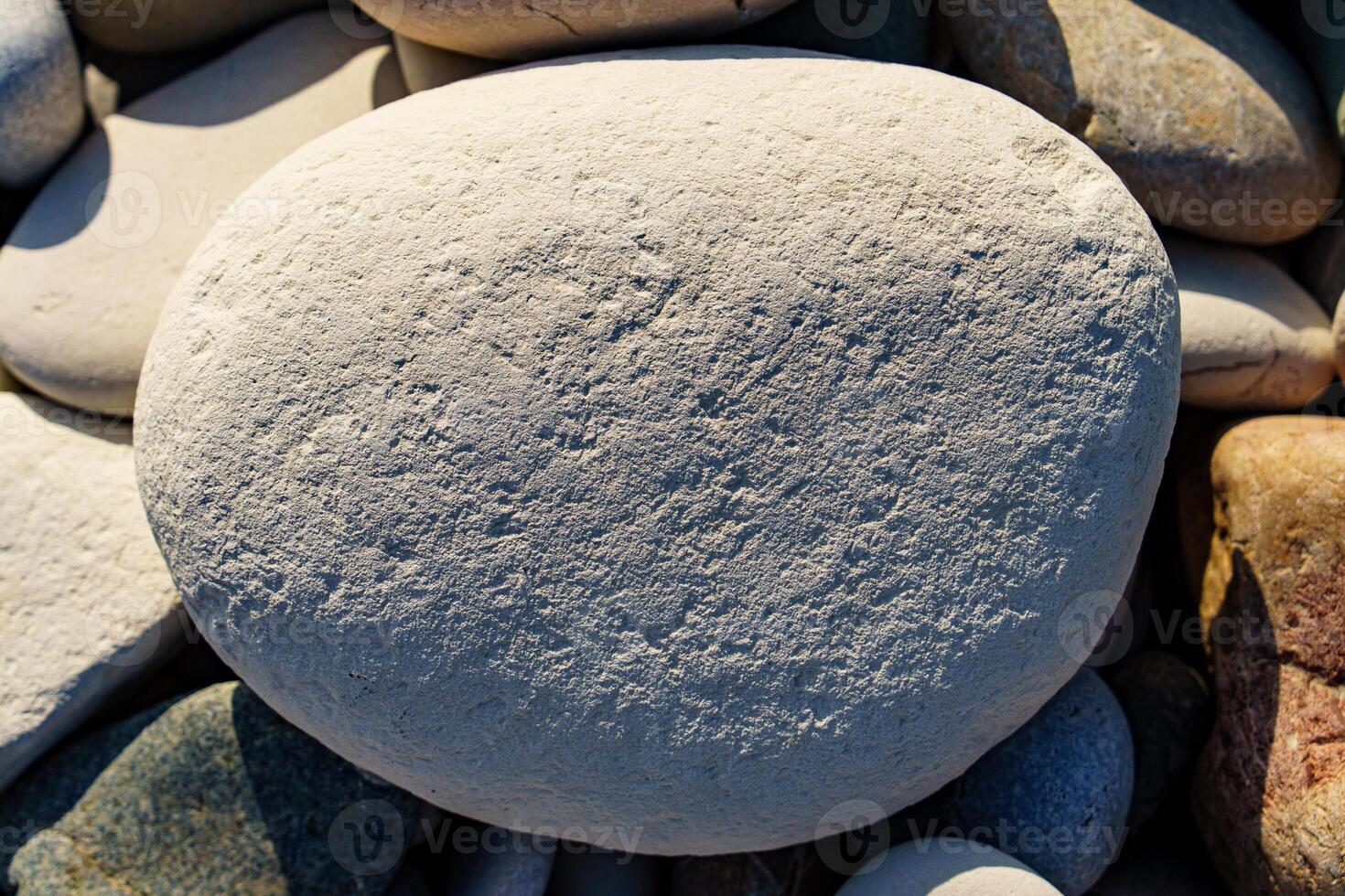 Large Smooth Stone Amongst Beach Pebbles in Natural Sunlight. Serene Beach Stone. photo