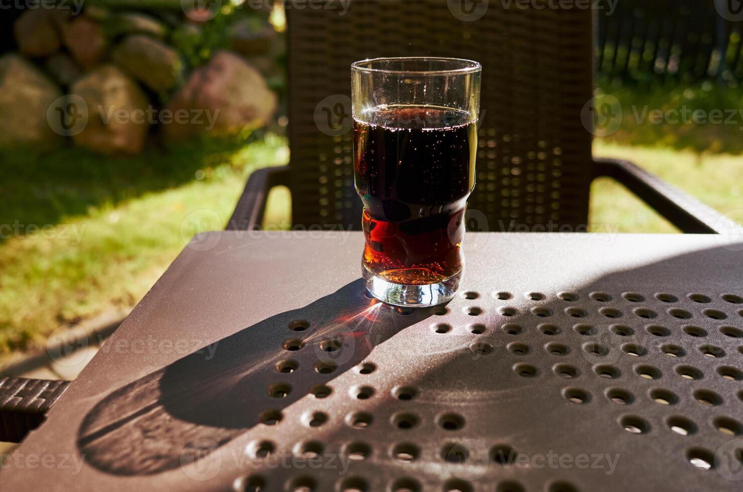 Glass of dark colored liquid sits on a table in the shade photo