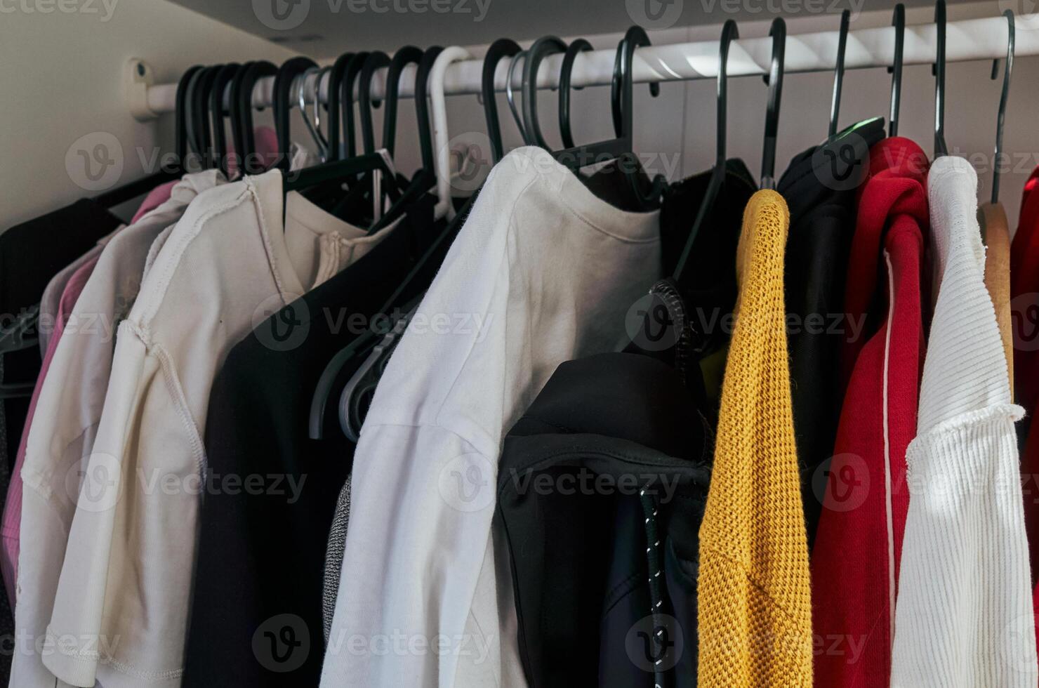 Closet full of clothes, including a white shirt and a red sweater photo