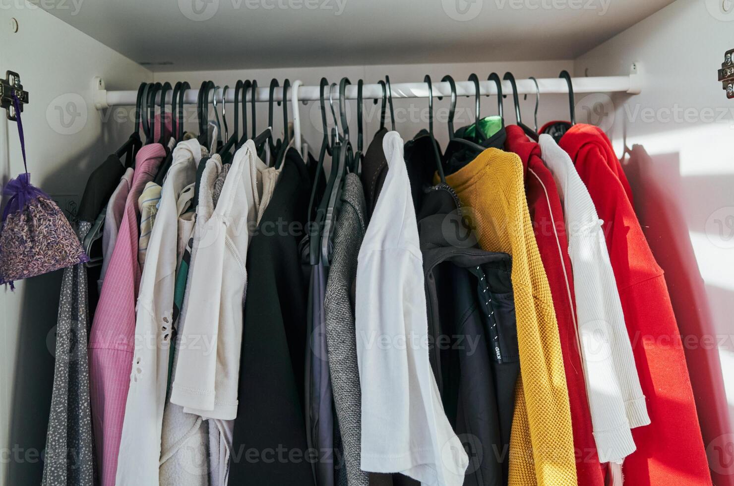Closet full of clothes with a purple bag hanging from the top photo