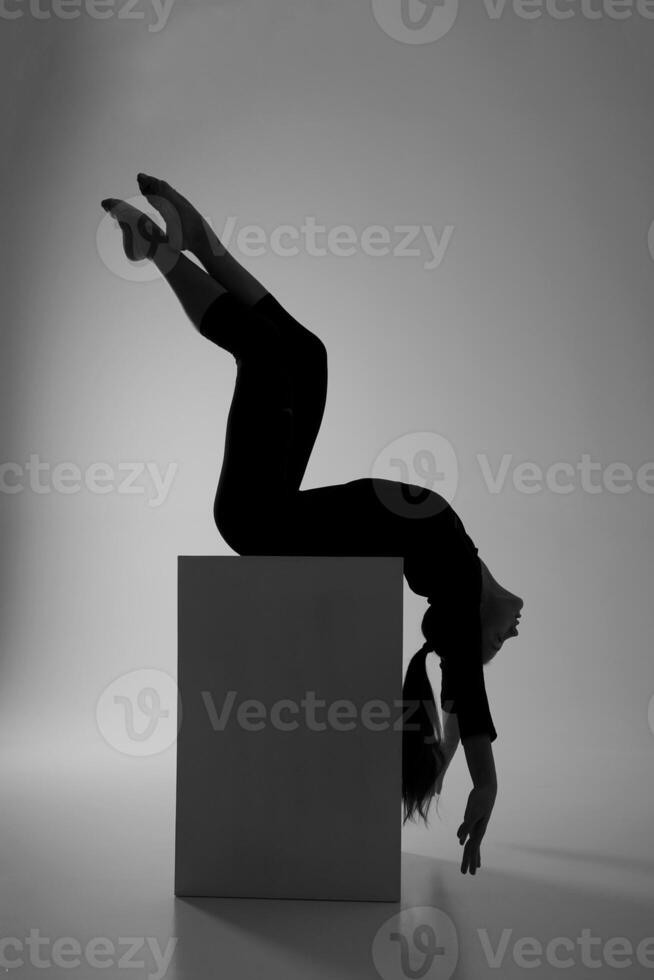 the silhouette of a girl from rhythmic gymnastics in a bodysuit on a cube in a deflection photo