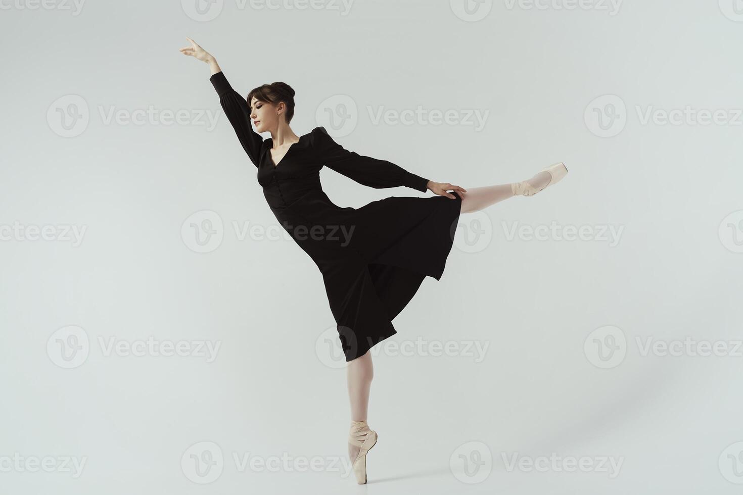 ballerina in a black dress and ballet shoes poses in a photo studio in motion showing beautiful long legs make attitude