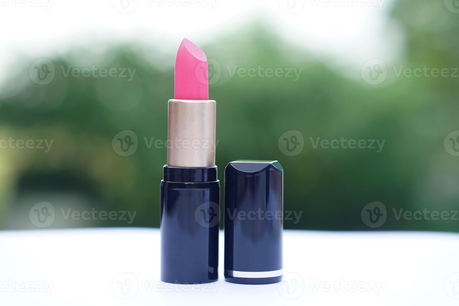 A single pink lipstick in a sleek black and gold tube, placed on a white surface with a soft green background. Concept, beauty , cosmetic, skincare branding, or product showcases. photo
