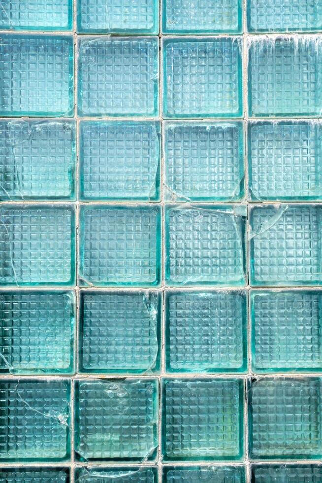 Transparent turquoise glass bricks with weathered surface texture showing interconnected cracks forming a chaotic pattern, vertical photo