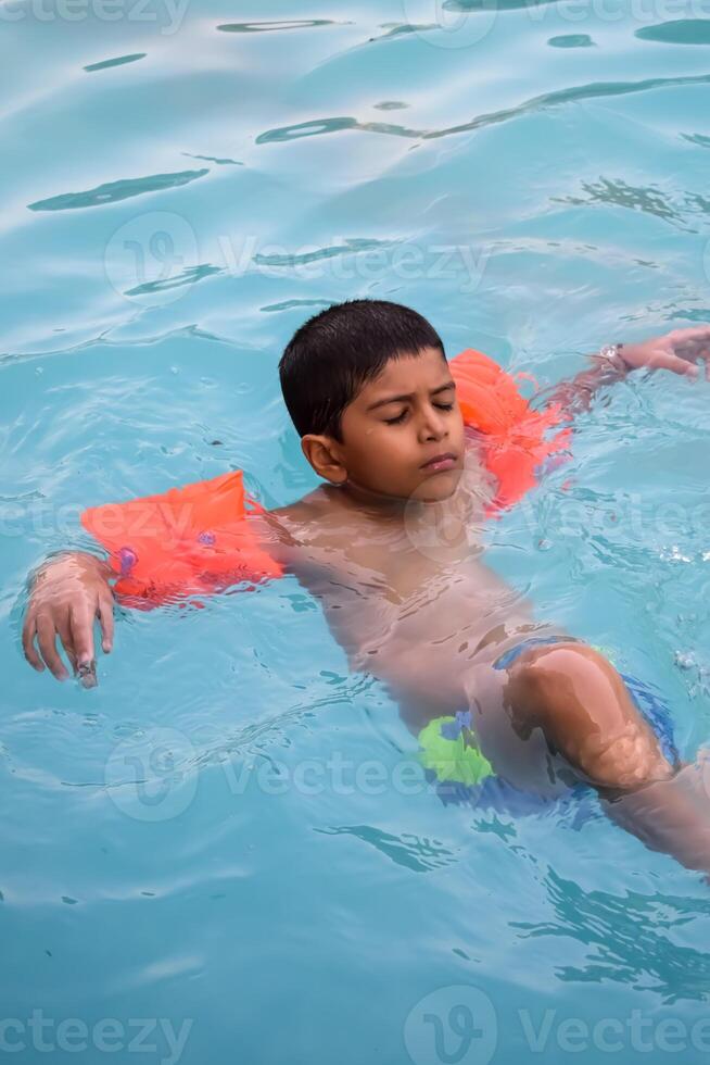 A young boy floating in a pool with his arms outstretched photo
