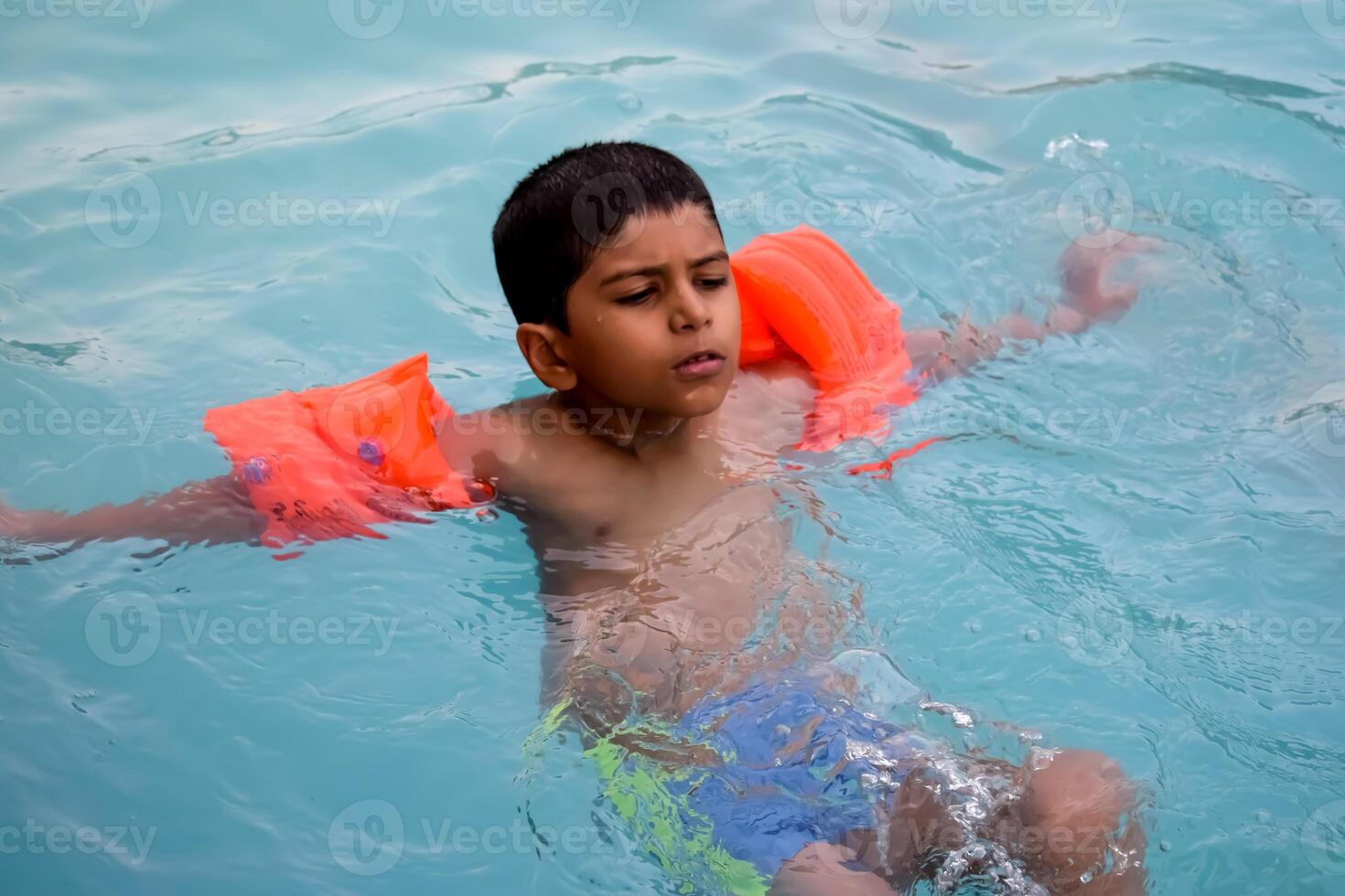A young boy floating in a pool with an orange life vest photo