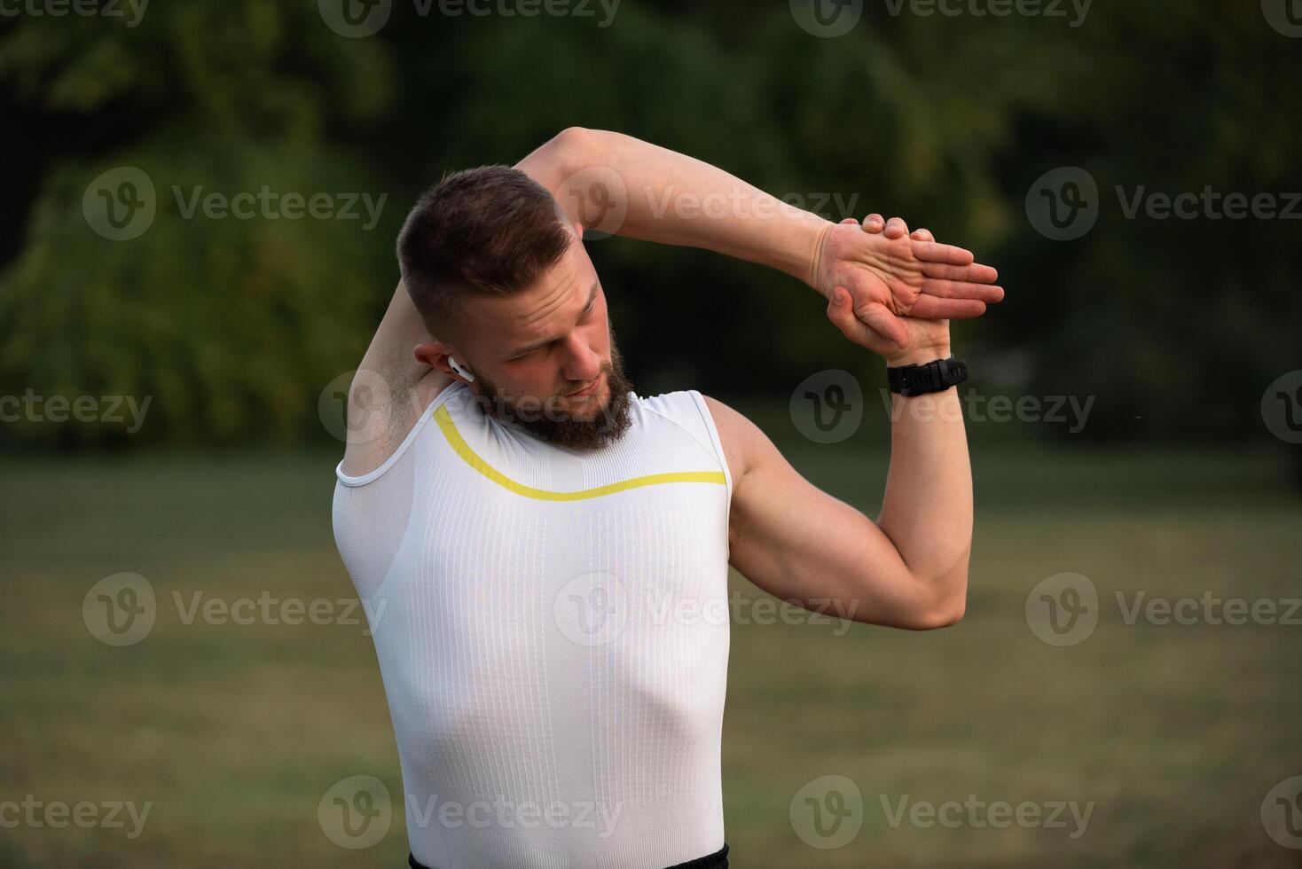 A young fit man doing stretching exercises before running or workout in a park. Active lifestyle, fitness and outdoor exercise concept. photo