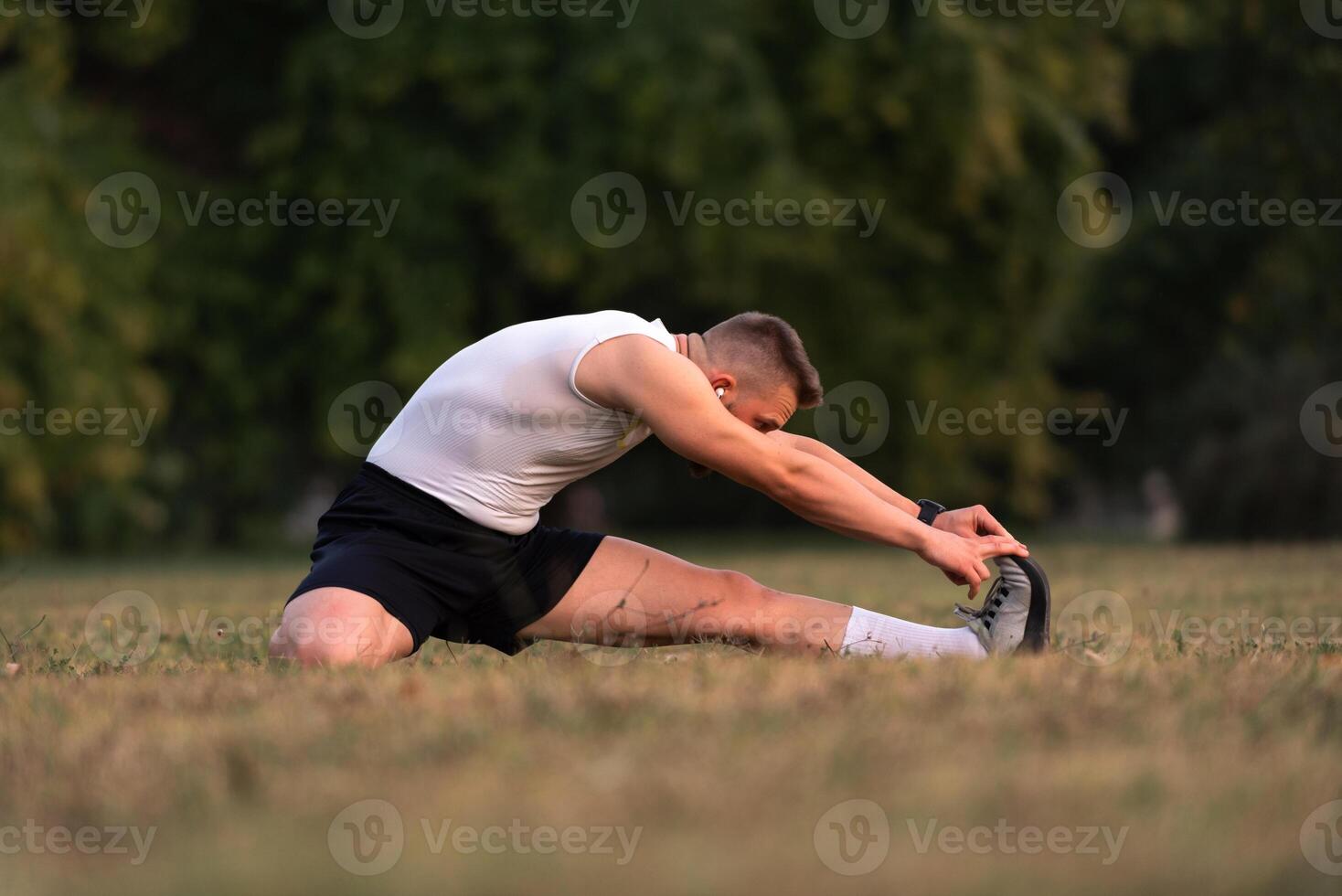 A fit man is doing stretching exercises before running or workout in the park. Outdoor fitness preparation, active lifestyle concept. photo