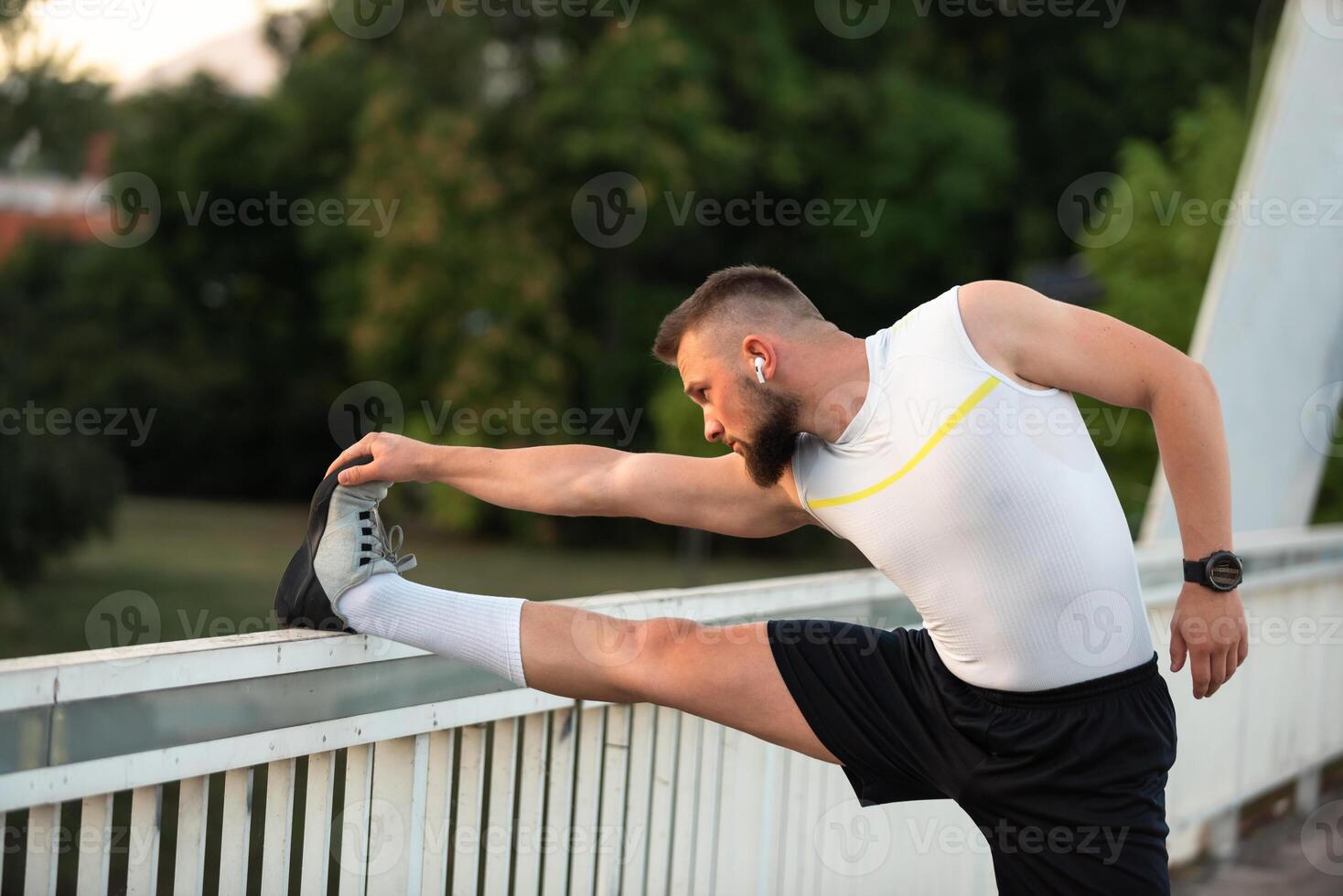 A young athletic man is doing stretching exercises before running or workout on a city bridge, Outdoor fitness preparation, active lifestyle concept. photo