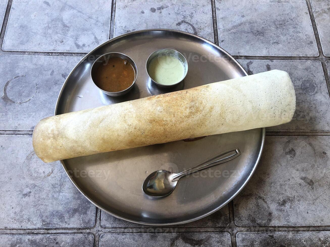 Indian masala dosa served with sambhar and chutney on a round metal plate. photo