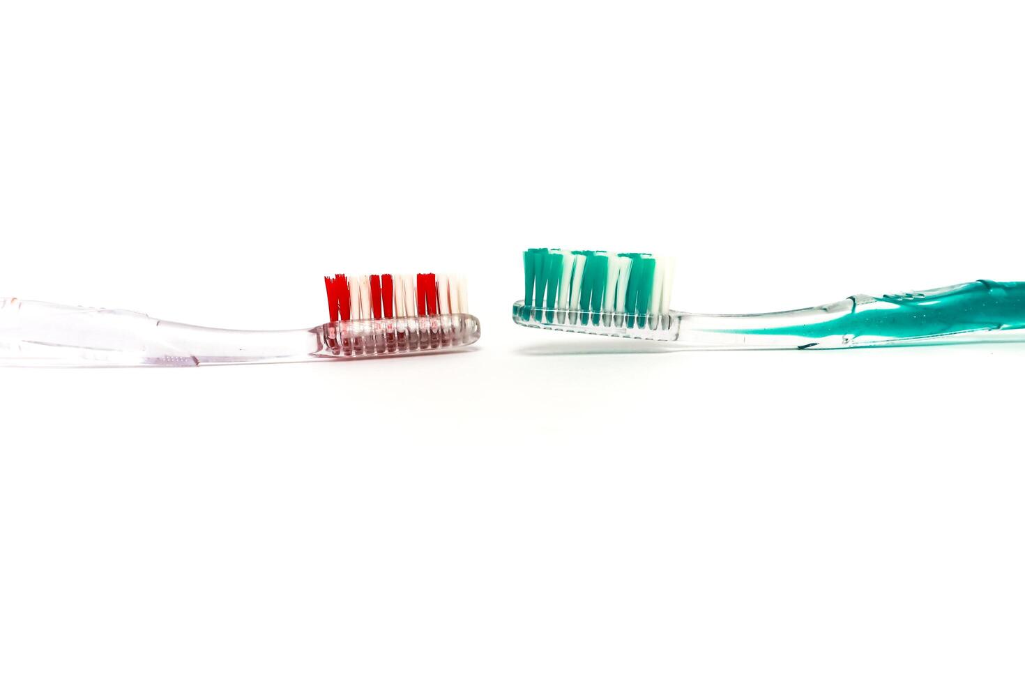 Two toothbrushes, one red and one green, face each other on a white background, oral health photo