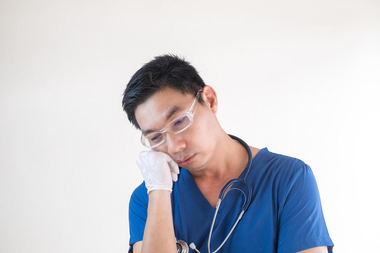 Exhausted Male Nurse in Scrubs Resting His Head on Hand photo