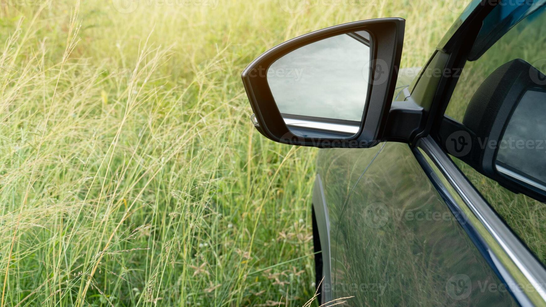 Abstract mirror view of the side of a navy blue car. Driving through the lush green grass. photo