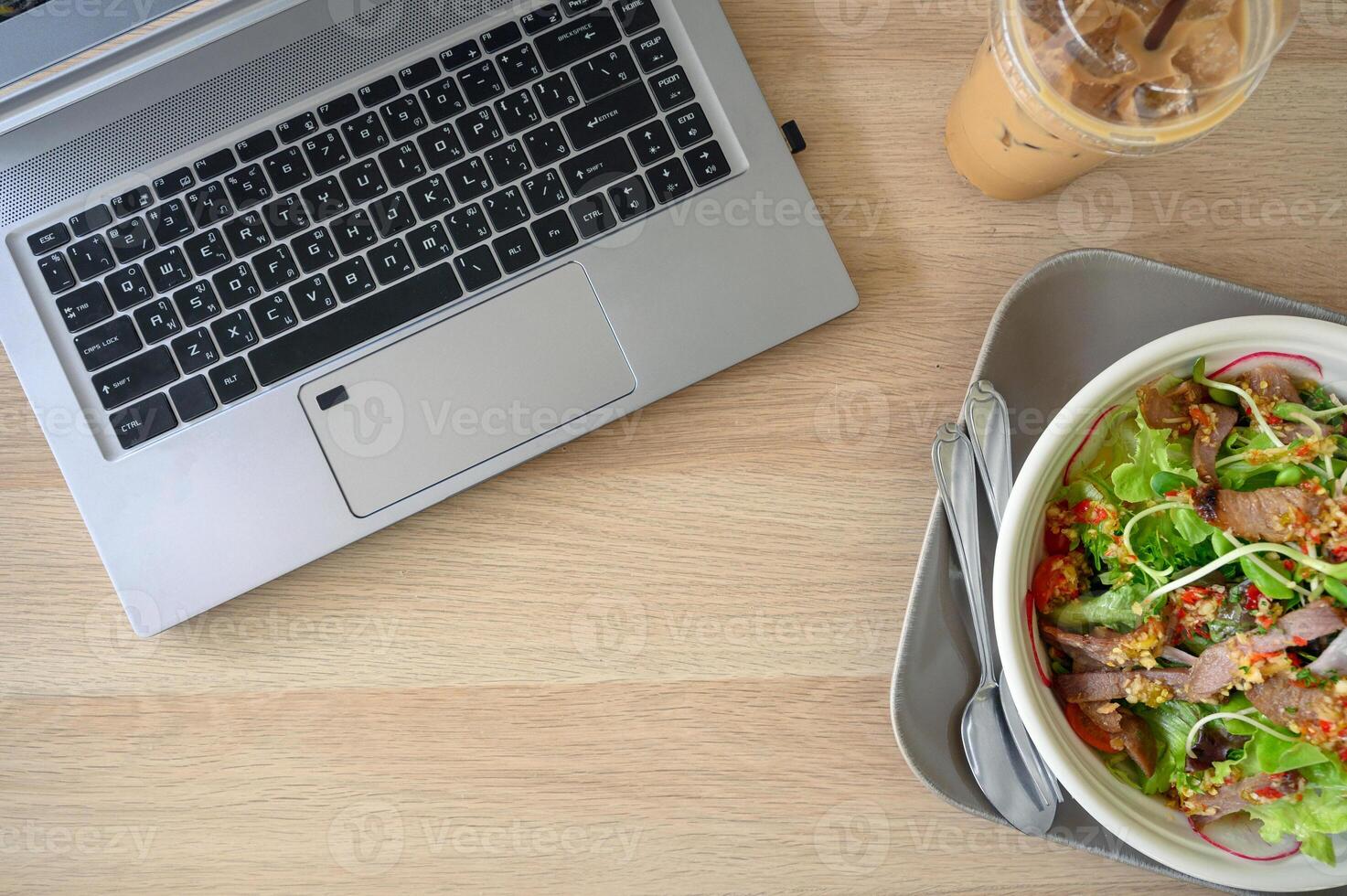 Modern laptop with spicy pork salad and ice coffee on wooden table photo