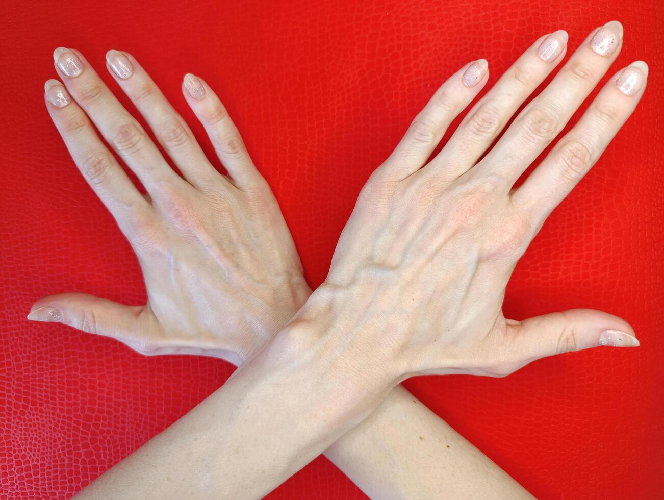 Crossed hands on a bright red surface showcasing elegant manicured nails in a creative position photo