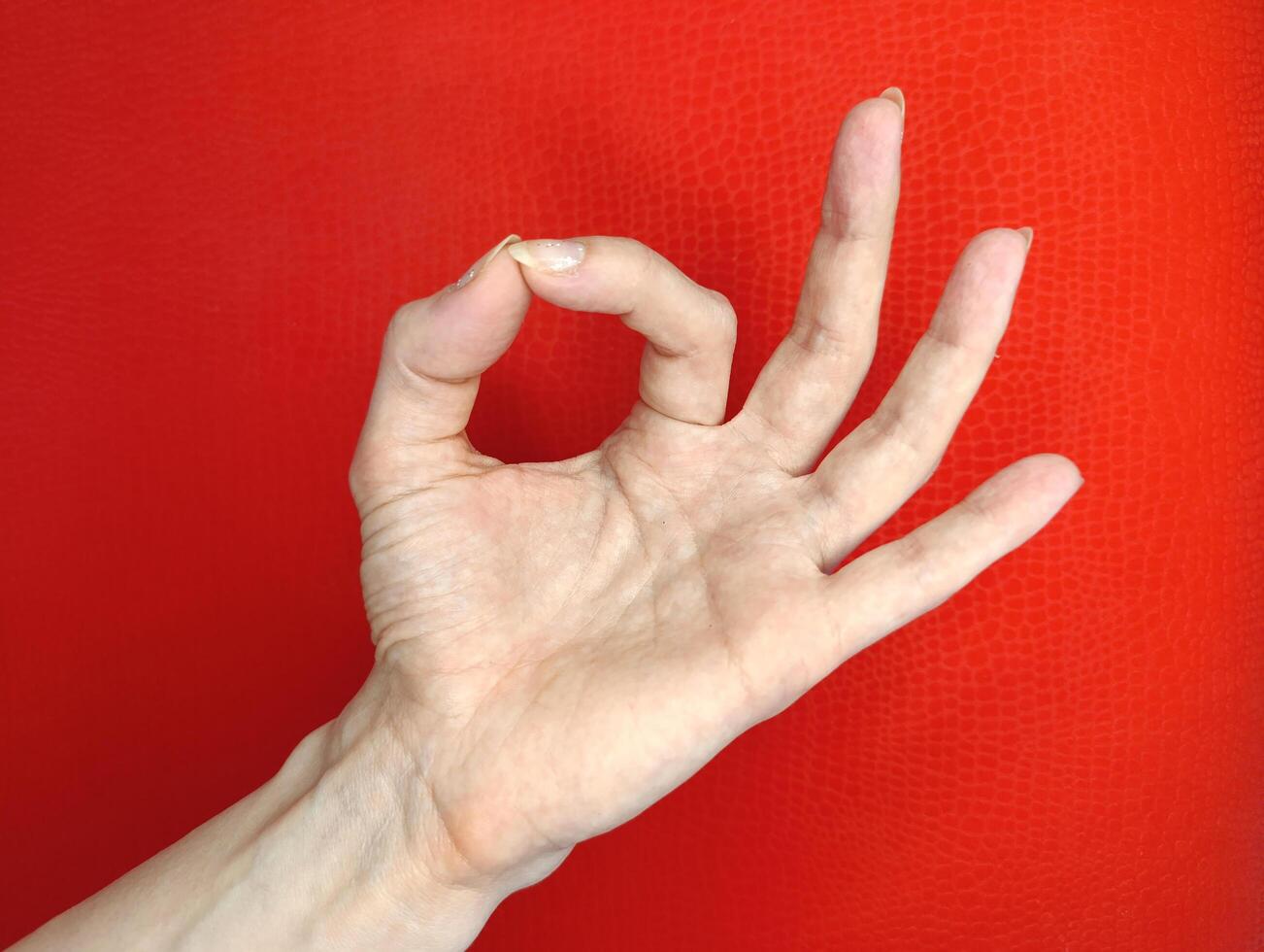 Hand showing okay gesture against a vibrant red background in a well-lit setting photo