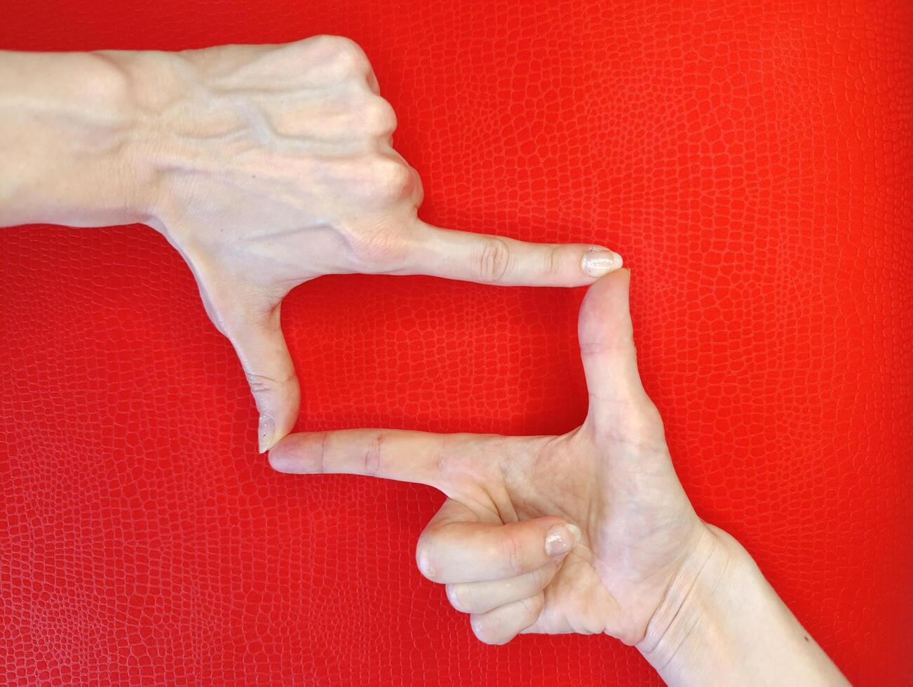 Hands framing a rectangular shape on a vibrant red background, highlighting a creative gesture in a playful atmosphere photo