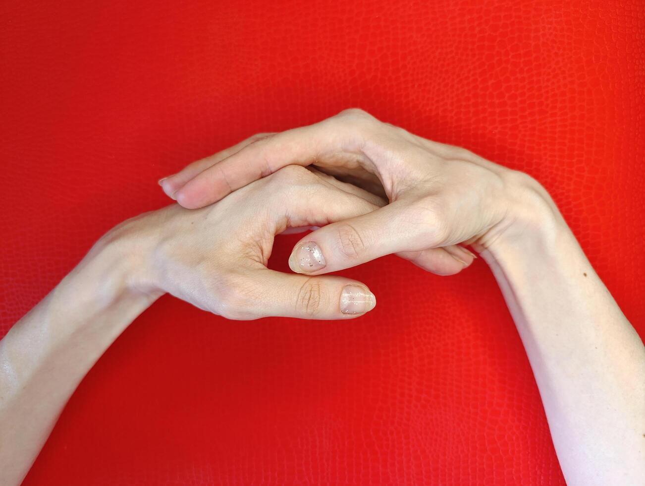 Hands clasped together on a vibrant red background, showcasing delicate fingers and detailed nail art photo