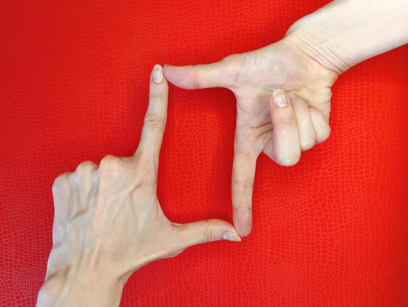 Creative hand gestures frame a square shape against a vibrant red background in a playful and artistic display photo