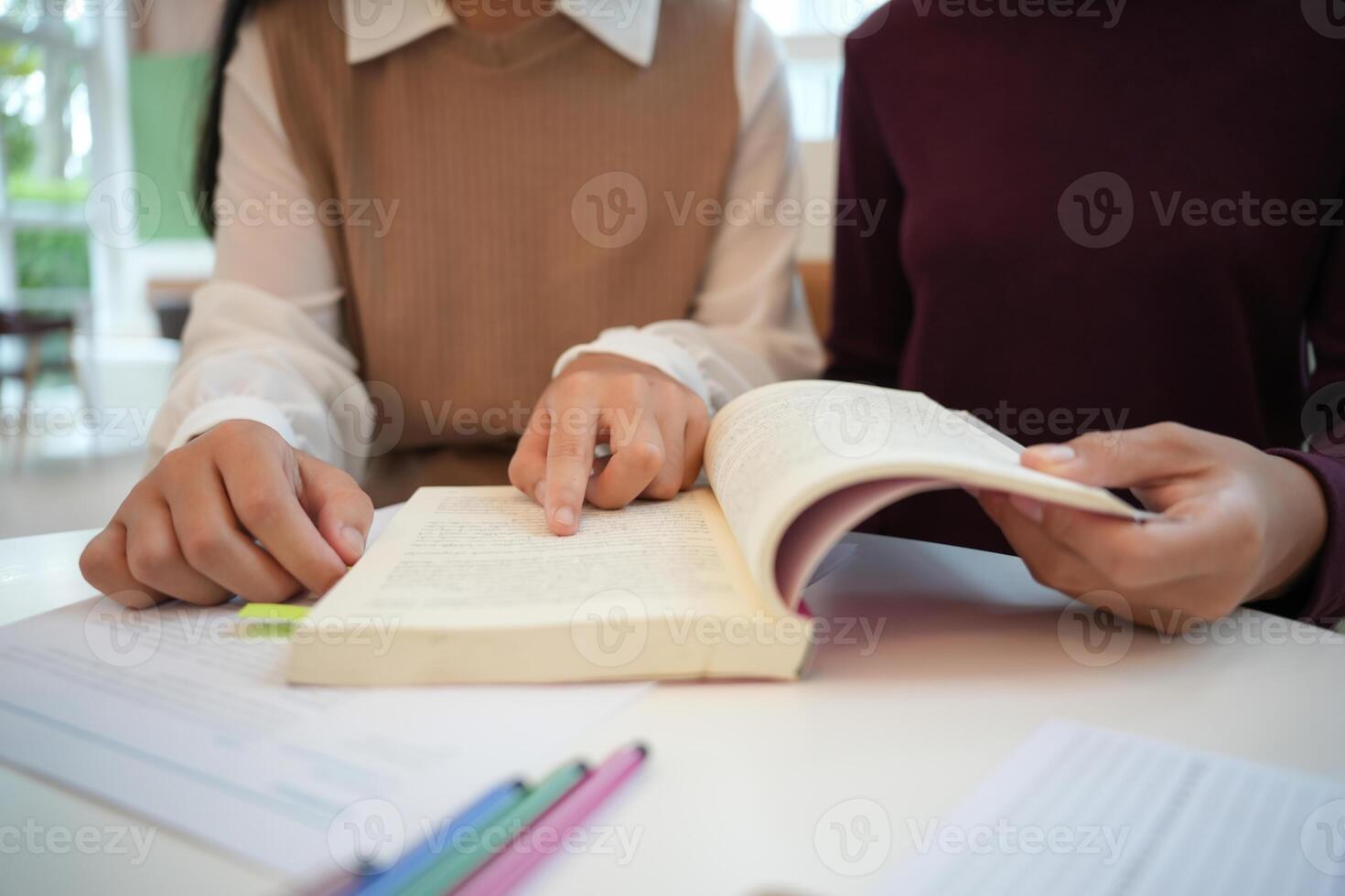 Learning with friends two people sitting at a table with a book and pencils photo