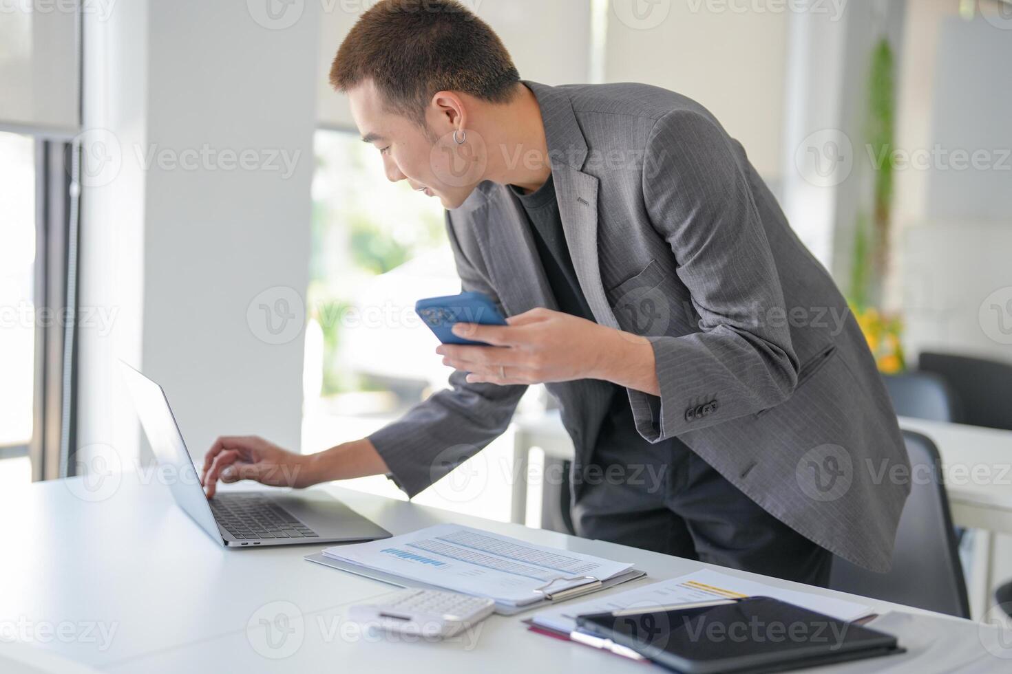 a businessman in a suit holding a cell phone and looking at his laptop photo