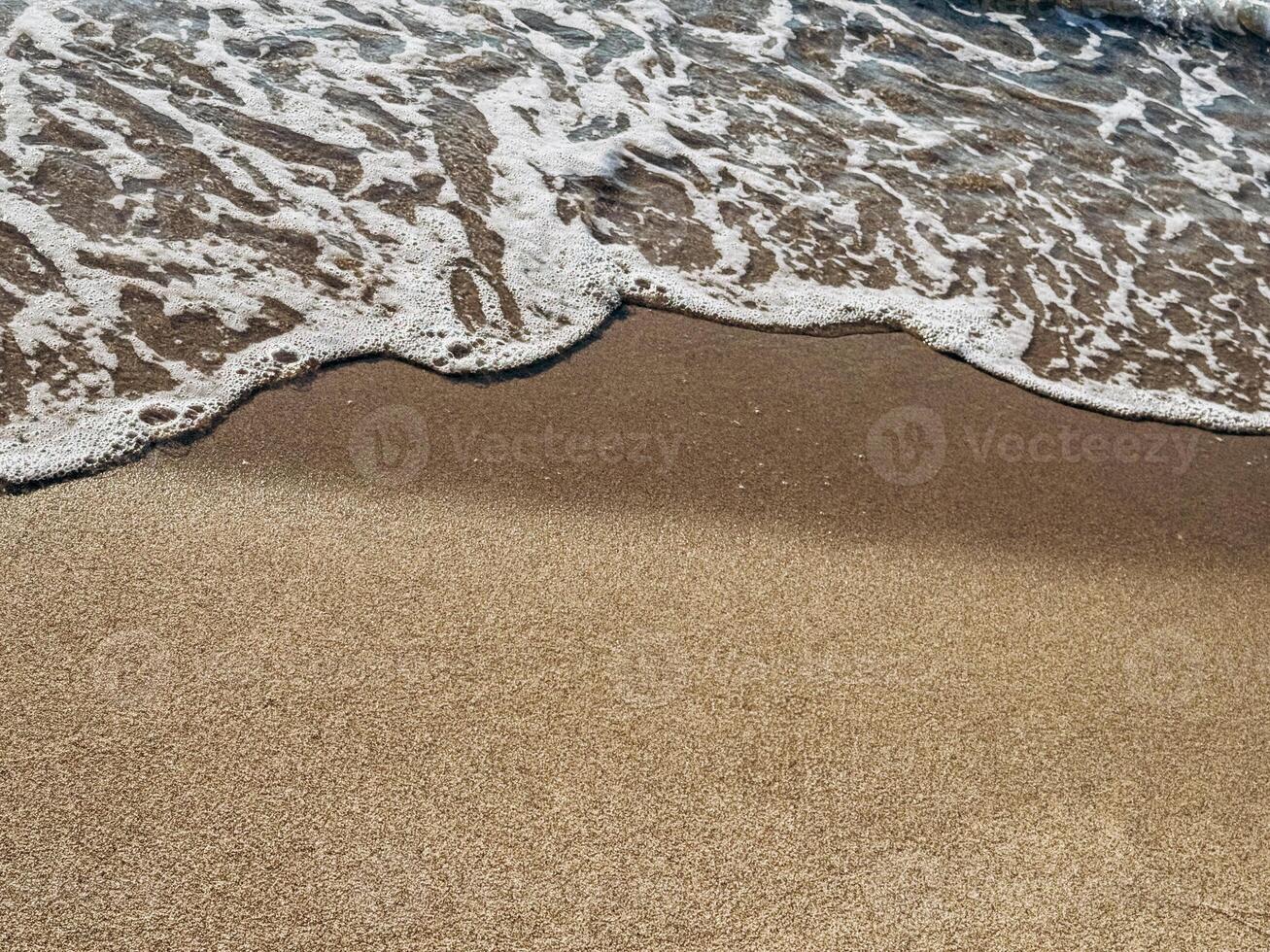 Ocean foam gently touching smooth brown sand surface in minimalist seashore abstract texture background Gentle ocean wave meeting smooth sand in calming symmetrical beach background ideal for wellness photo