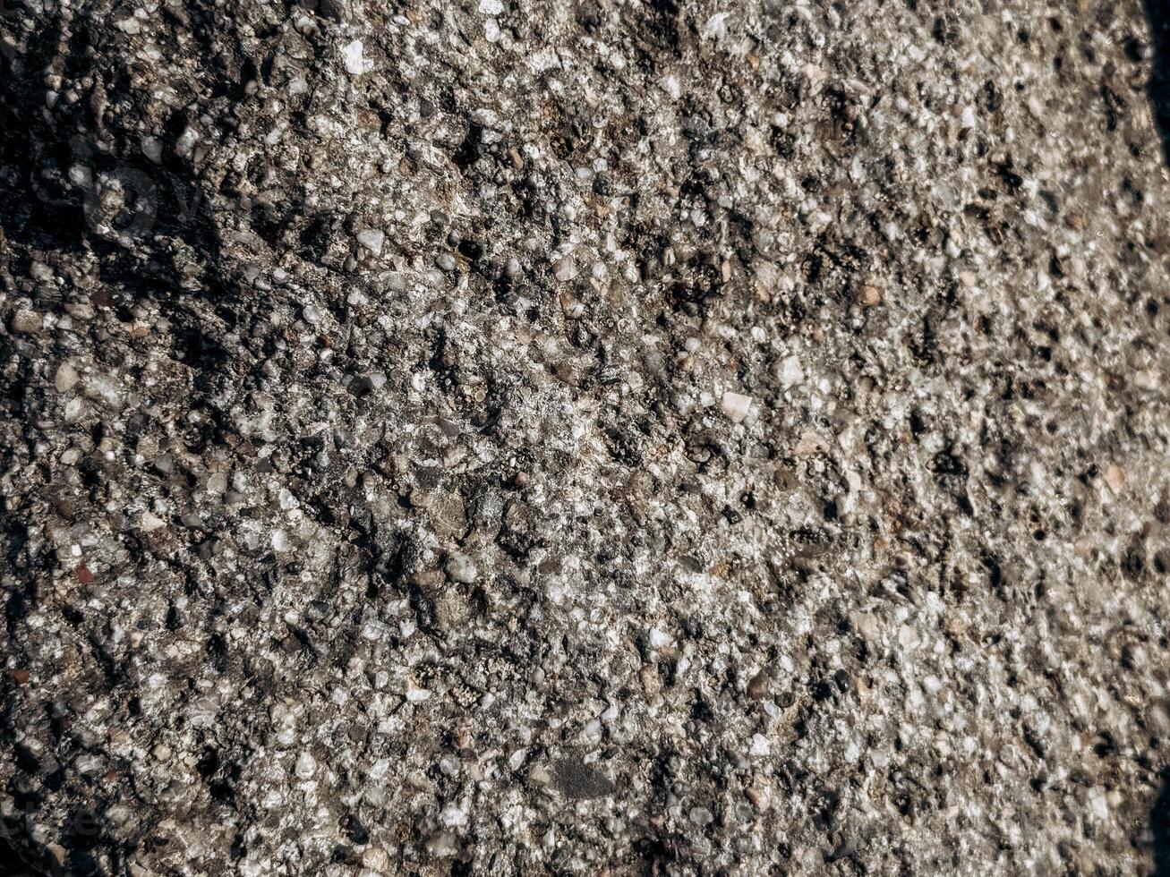 Macro view of urban asphalt filled with quartz and stone particles capturing raw textured pattern of pavement surface under natural sunlight photo
