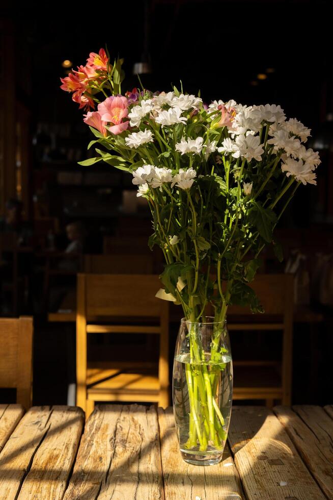 Bright flowers in a vase on a wooden table in a warm, inviting cafe setting during daytime photo