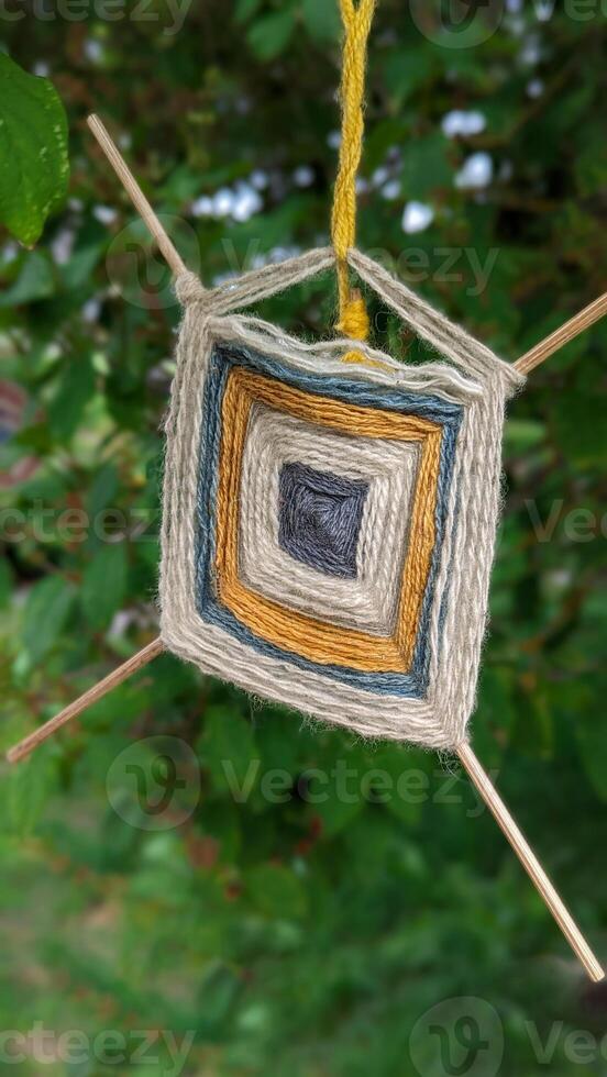 Handmade yarn ornament sways gently in garden tree, handmade details reflect folk roots and mindful art, handmade craft brings cozy spirit to natural surroundings. photo