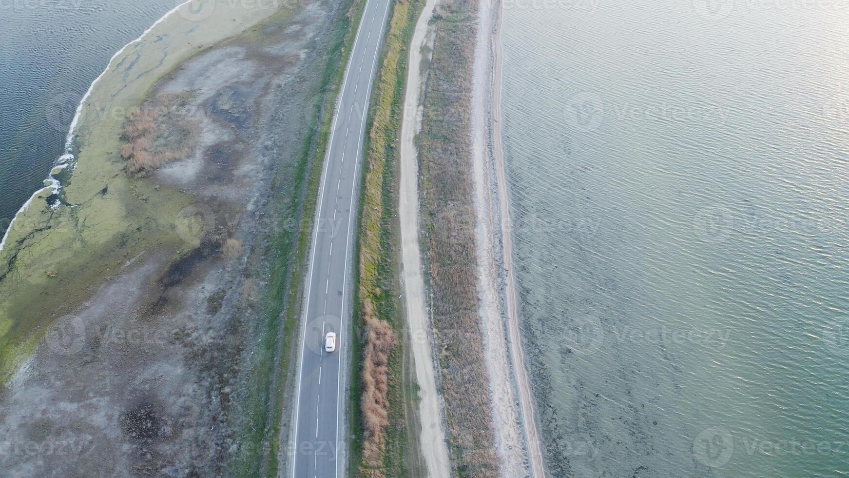 top down view of a lone white car driving on a rural highway surrounded by lakes. photo