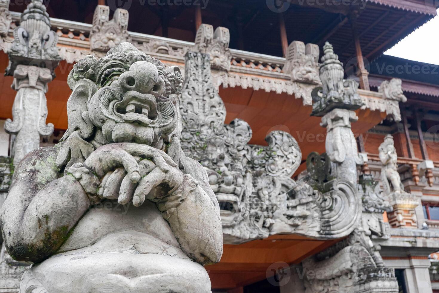 Traditional Balinese stone statue in front of intricately carved temple architecture in Bali, Indonesia. Cultural heritage and Asian spiritual art. photo