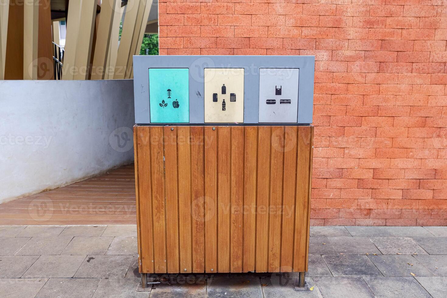 Modern recycling bin with three compartments for organic, plastic, and non-organic waste. Eco-friendly wooden design in a public space with brick wall background. photo