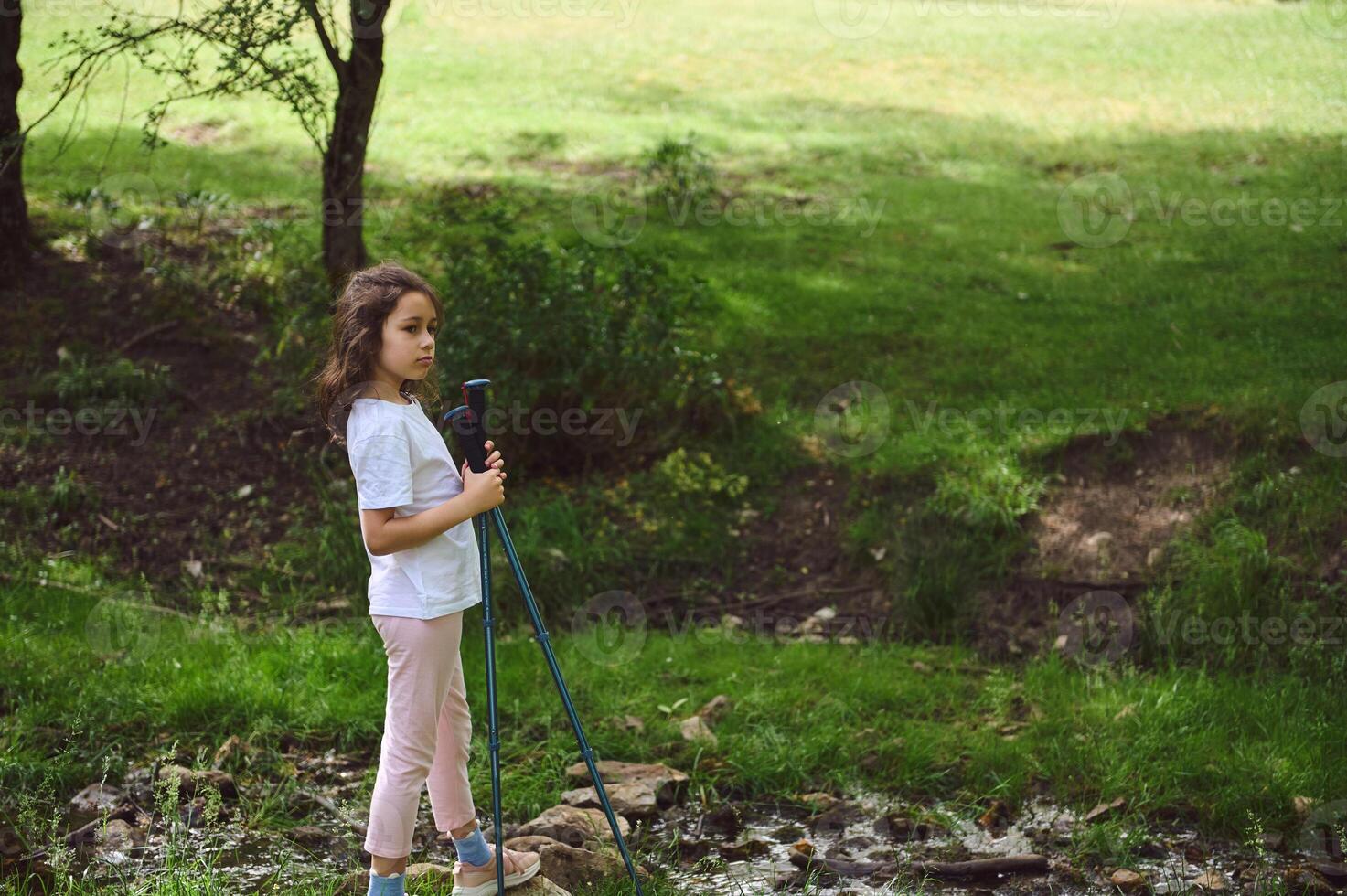 Young Girl Exploring Nature with Poles in Scenic Countryside Setting photo