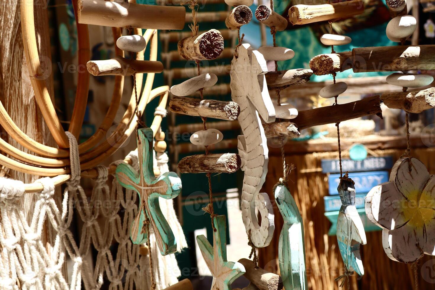 Handmade beach-themed wooden decorations, including a seahorse, crosses, and tropical elements, hang in bright sunlight at a coastal craft market. photo