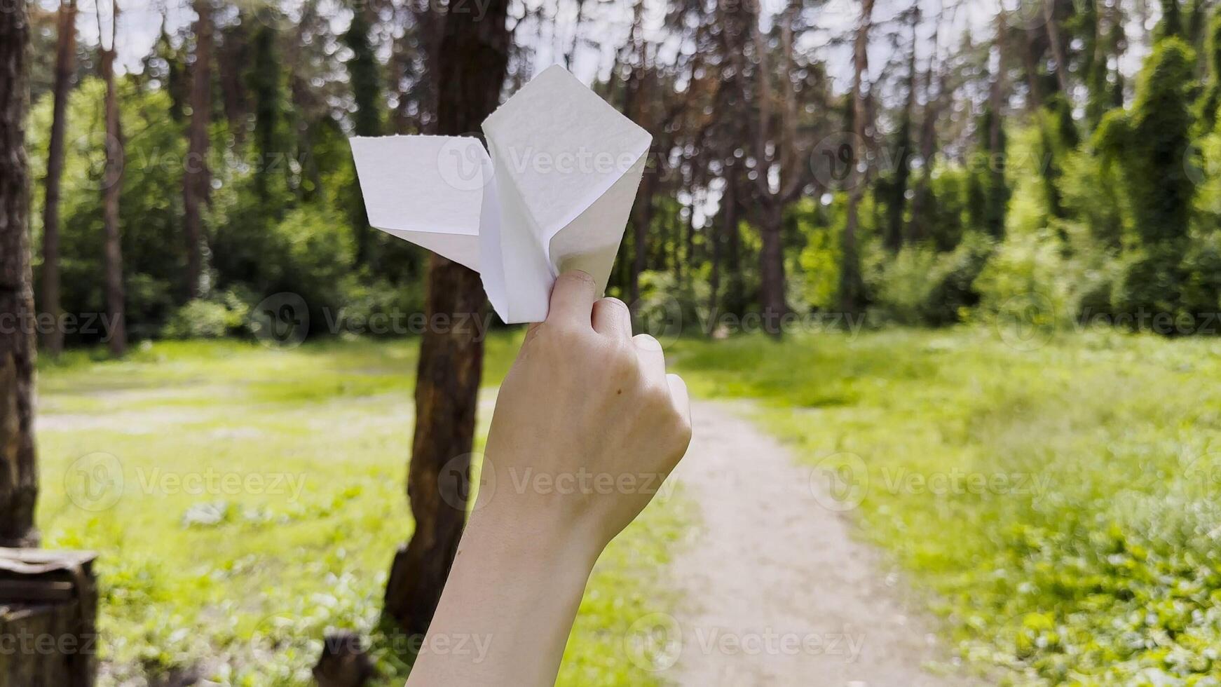 Female hand playing with paper airplane at summer forest.Girl walking with toy plane at woodland on sunny day. Young woman having fun at nature. Concept of leisure outdoor. Close up photo