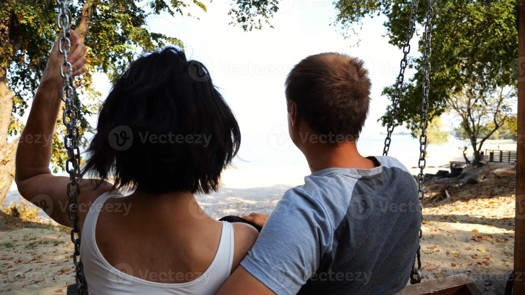 Romantic couple ride on swing together at sea beach.Happy lovers enjoy to spending time together at resort. Carefree pair enjoying rest near ocean at sunny day. Concept of summer vacation or holiday photo