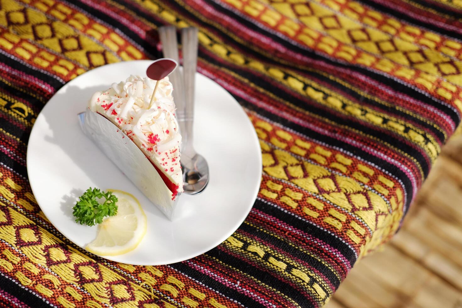 Homemade fresh strawberry cheese cake with lemon piece in white dish on Thai native pattern tablecloth in natural sunlight in tropical cafe photo