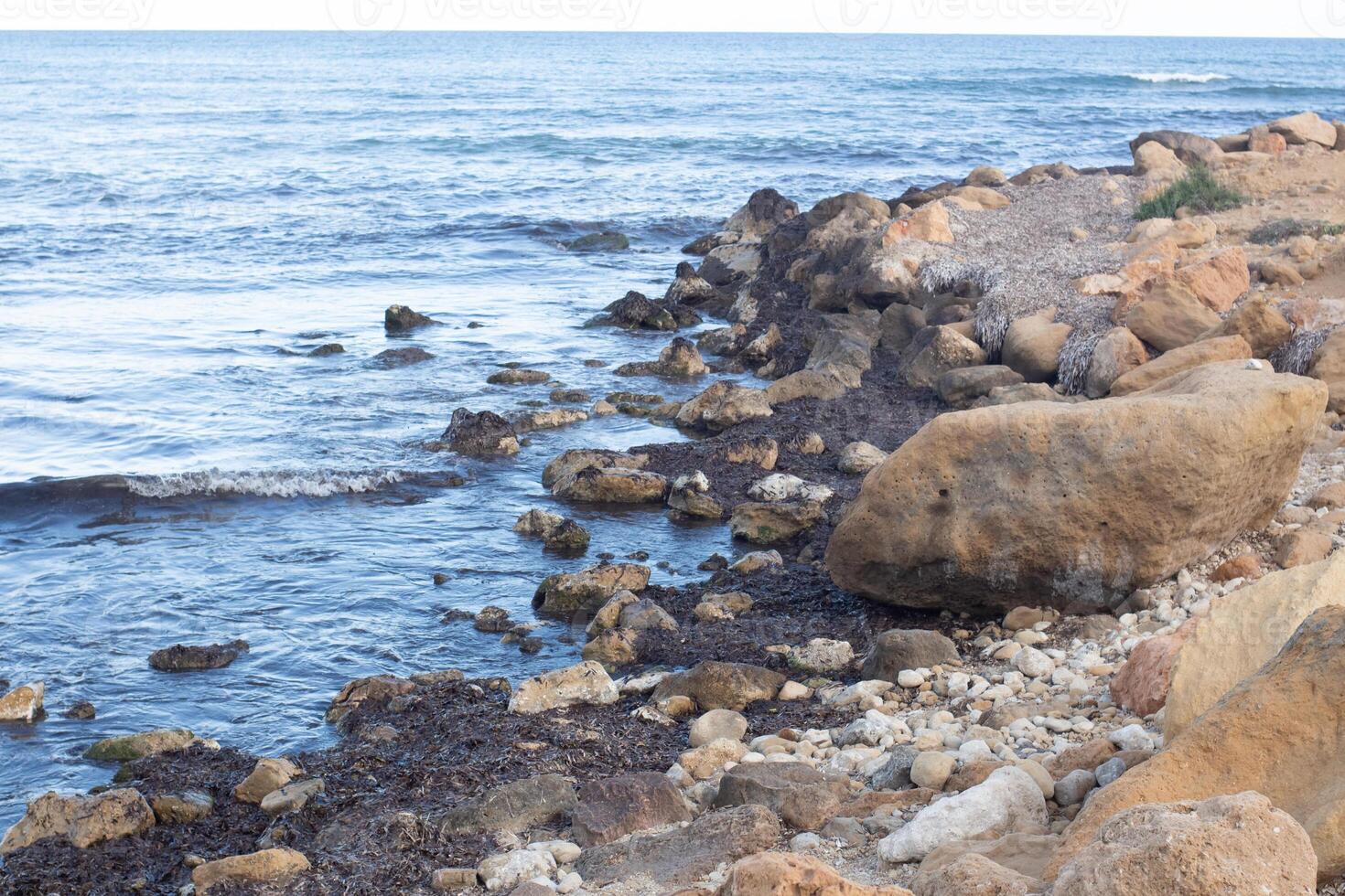 Explore the serene coastal landscape of Spain with rocky shores and calm ocean waves under a clear sky photo