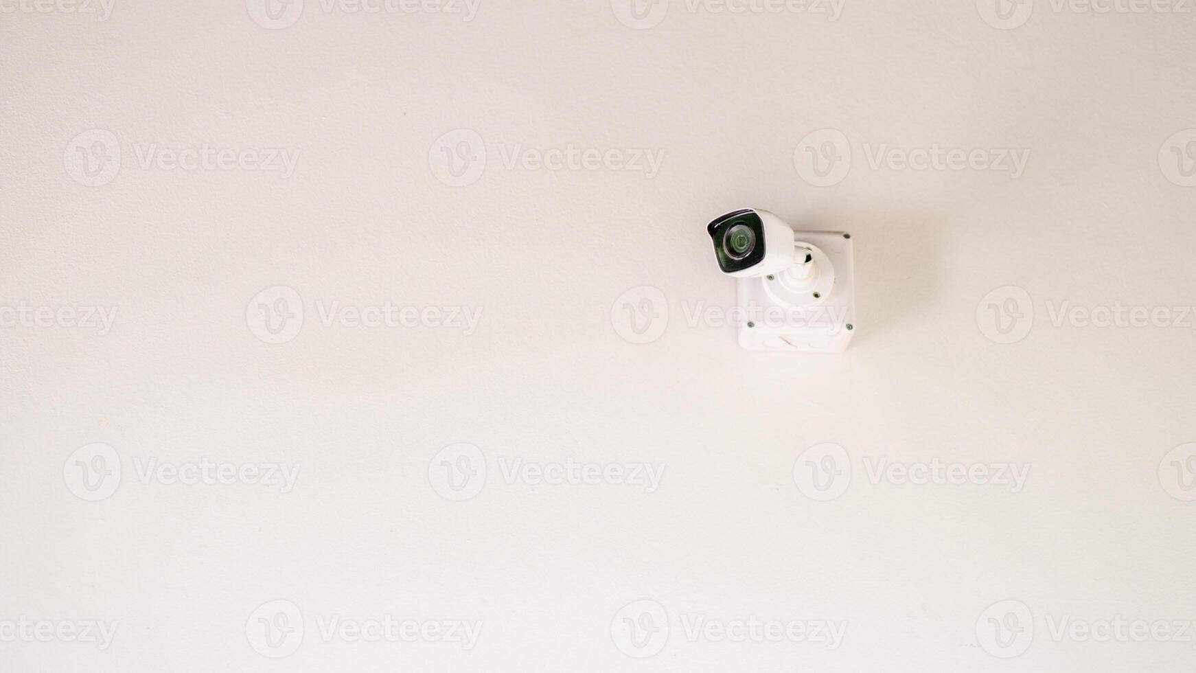 A sleek security camera mounted on a white ceiling, showcasing modern surveillance technology in a minimalist setting. photo