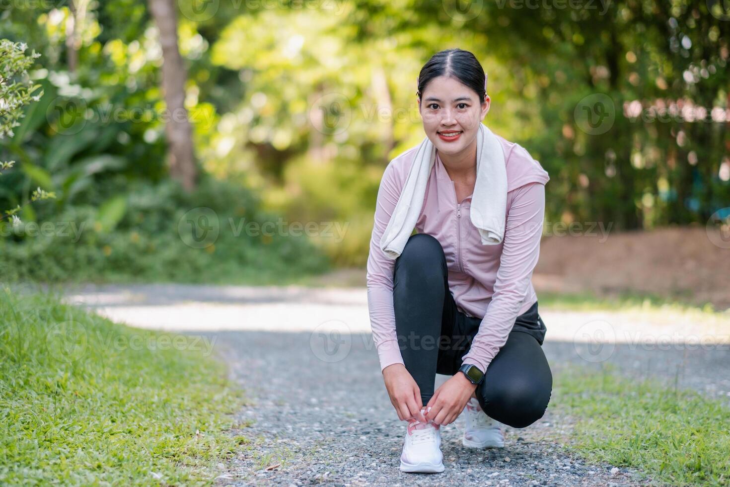 A woman prepares for a run by tying her shoelaces on a scenic park trail surrounded by greenery. photo