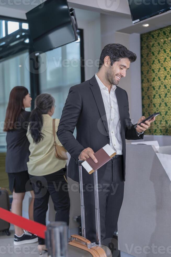 smiling businessman in suit one hand suit carry the suitcase and holding passport,other hand using smartphone,passengers getting service in the airport photo