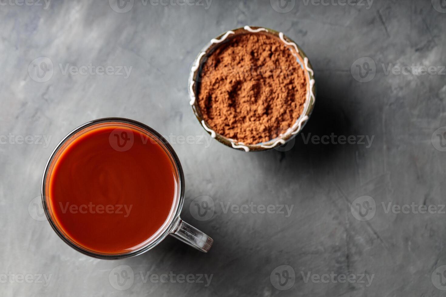 Hot Chocolate Drink in Glass Mug with Cocoa Powder in Blue Bowl on Gray Concrete Surface photo