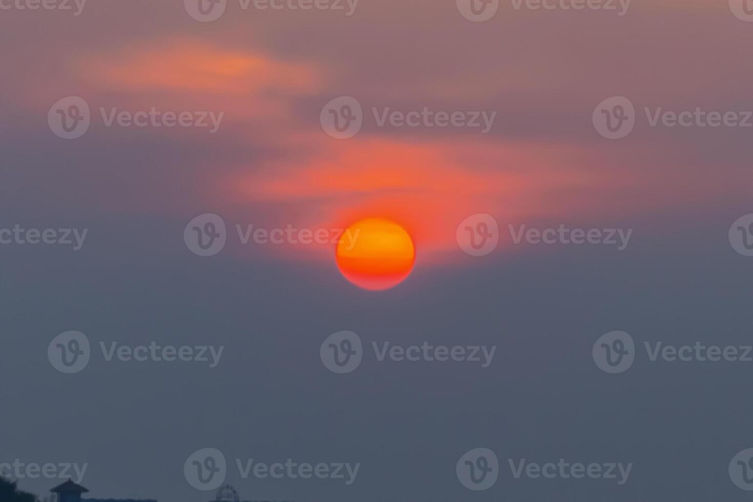 Beautiful sunset over the sea with glowing orange sky and silhouettes of trees and houses. Calm and dreamy photo