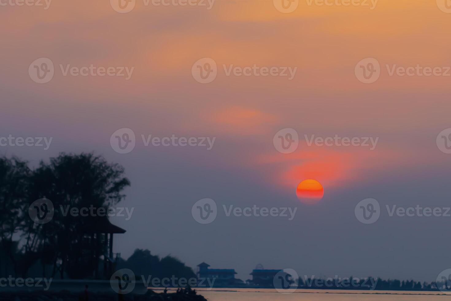 Beautiful sunset over the sea with glowing orange sky and silhouettes of trees and houses. Calm and dreamy coastal atmosphere photo