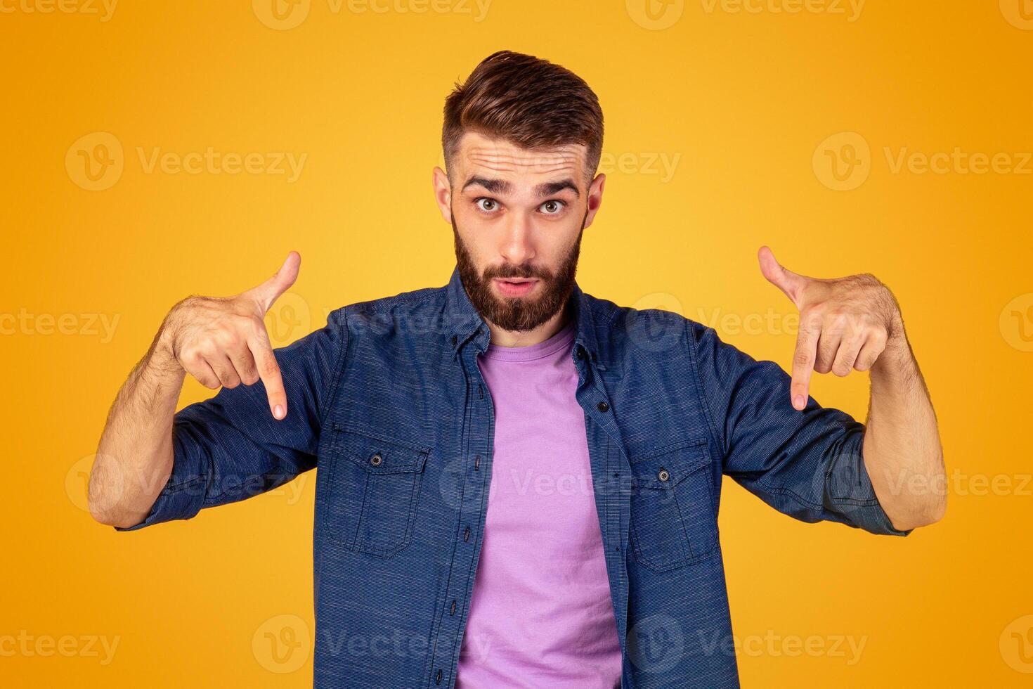 Surprised bearded guy pointing downwards on orange studio background, panorama. Emotional Caucasian guy showing or advertising something, offering big sale or product promotion photo