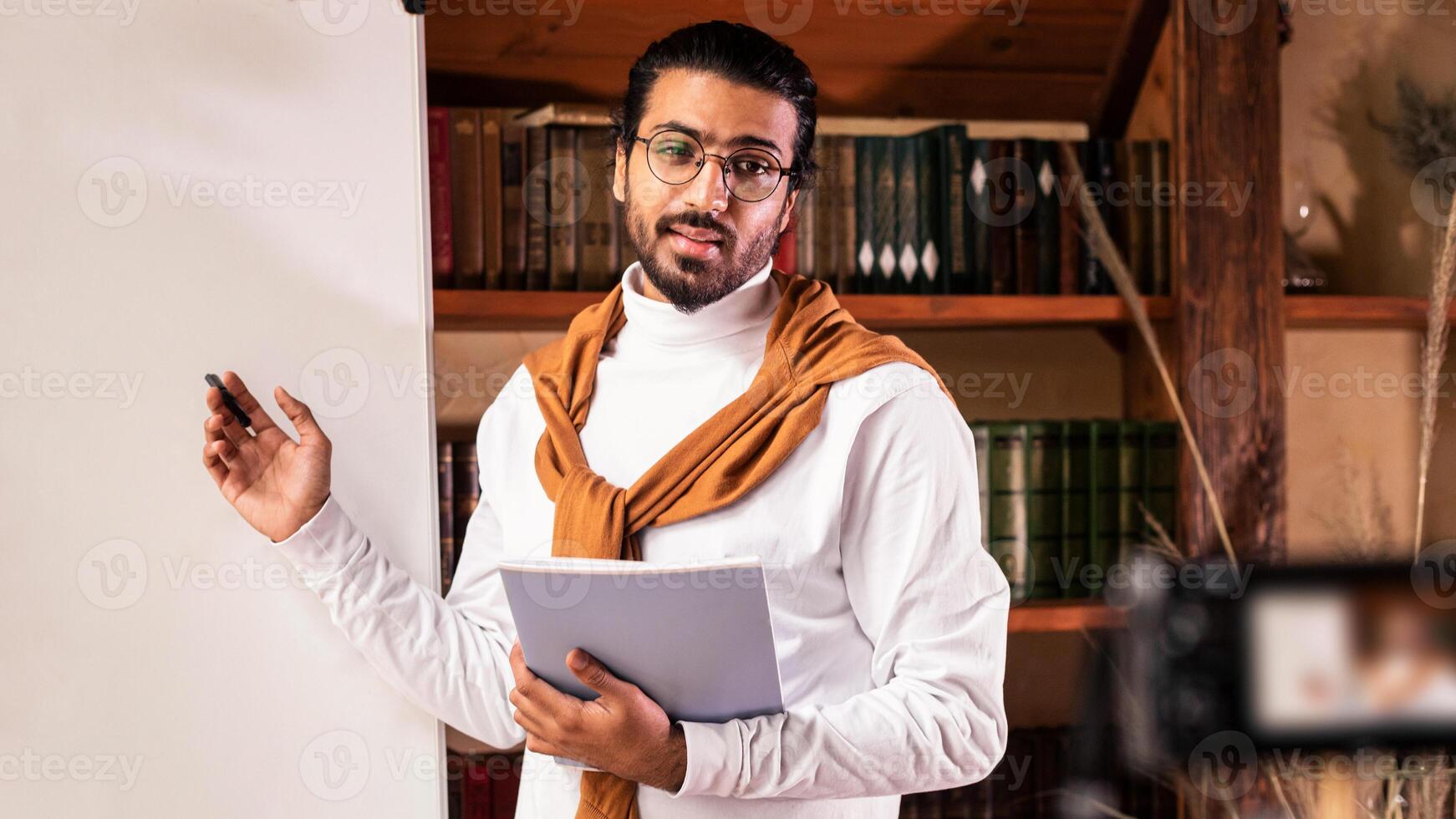 E-Teaching. Indian Teacher Guy Teaching Online Standing Near Blackboard Explaining English Language Grammar Looking At Camera Indoor. Remote Teaching And E-Learning, Education Concept photo